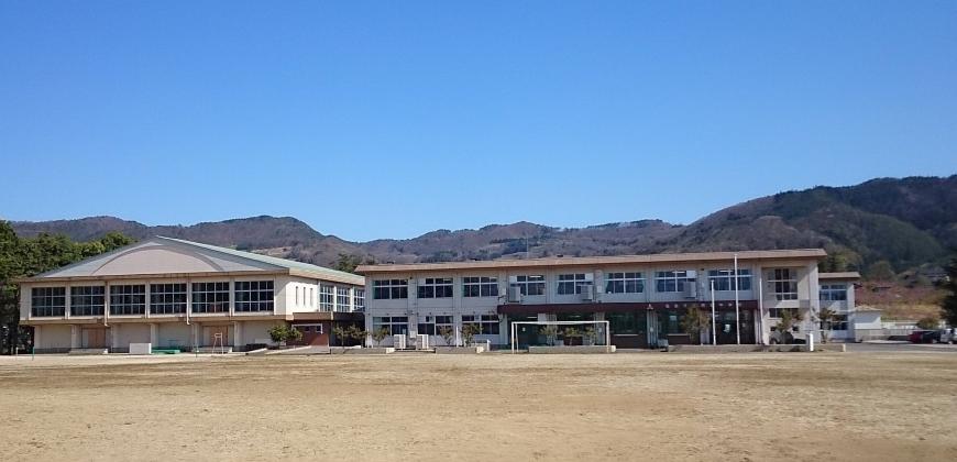 体育館の右側に2階建ての校舎がある西根中学校をグラウンドから撮影した写真