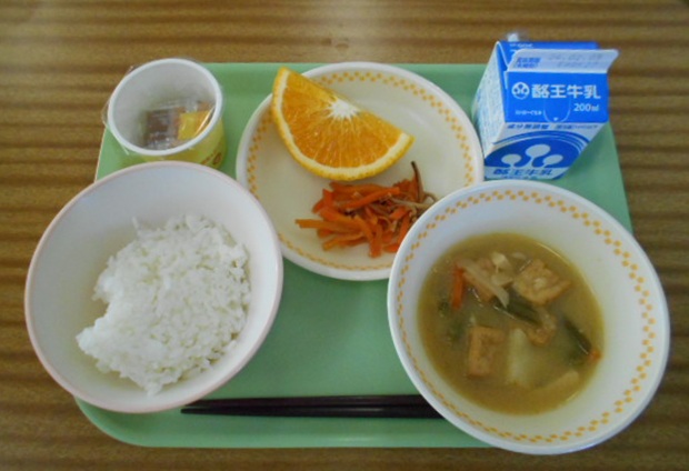 お盆にごはん、スイートスプリング、いか人参、凍み豆腐のみそ煮、納豆、牛乳、箸がのった給食の写真