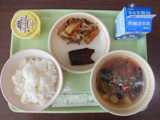 若草色のトレーの上に、ごはん、こづゆ風汁物、にしんのかんろ煮とぜんまいの炒め煮が盛り付けられた皿、パックの牛乳、プリンが乗っている写真