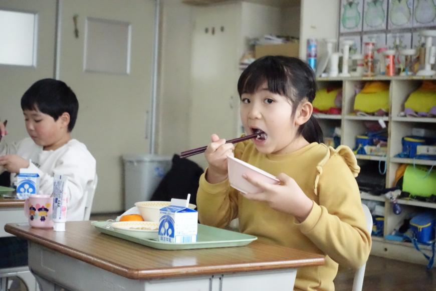 給食を口に運ぶ女子生徒の写真
