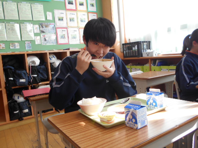 汁椀を持って食べている男子生徒の写真