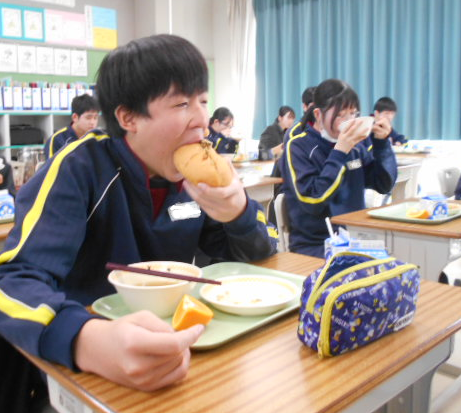 給食の焼きそばパンにかぶりつく男子生徒の写真