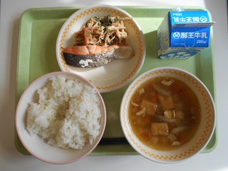 若草色のトレーの上に、カルシウムごはん、ざくざく汁、さけの塩焼きとじゅうねんごまあえが盛り付けられた皿、パックの牛乳が乗っている写真