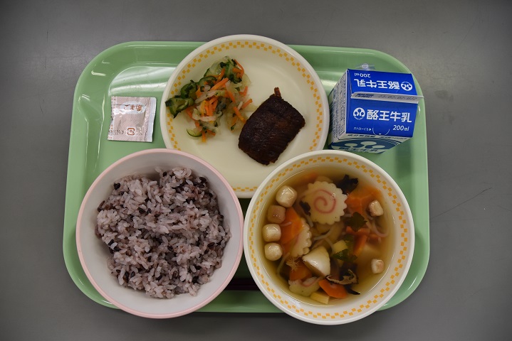 若草色のトレーの上に、紫黒ごはん、こづゆ、にしんのかんろ煮と野沢菜和えが盛り付けられた皿、パックの牛乳がのっている写真