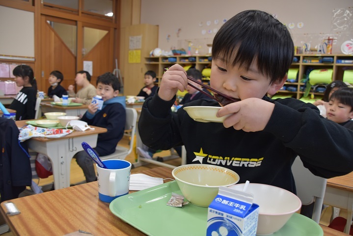 お皿を持ち上げてにしんの甘露煮を食べている男子児童の写真