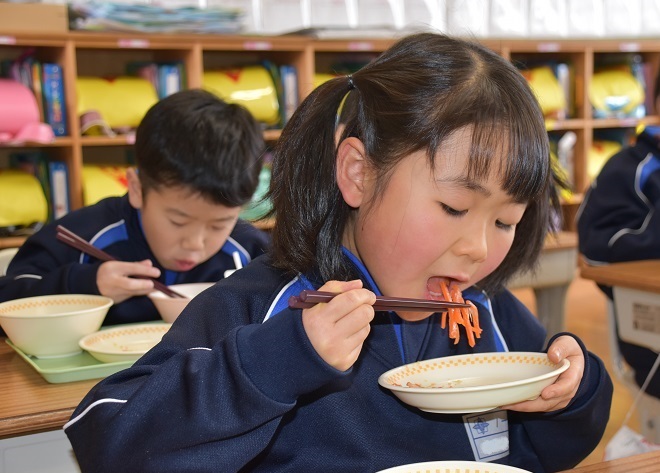 お皿を持っていかにんじんを食べている女子児童の写真