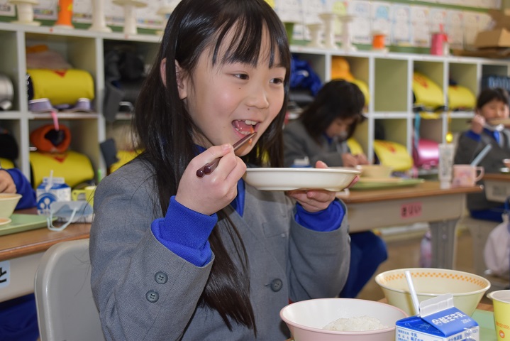 お皿を持ち、いかにんじんを食べている女子児童の写真