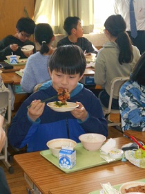 嬉しそうな顔で鶏肉のみそ焼きを食べている男子生徒の写真