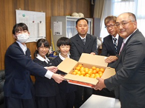 生徒3人と関係者3人がたくさんのみかんが入った箱を持っている写真
