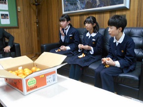 生徒3人が椅子に座って話を聞き名がらみかんを食べている様子の写真
