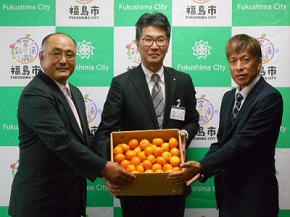男性3人がたくさんのみかんが入った箱を持って記念撮影をしている写真