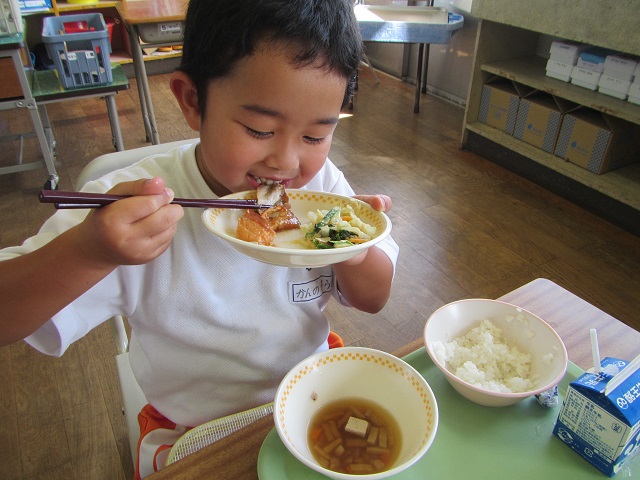 男の子が皿を持ち鮭の西京焼きを嬉しそうに口に運んでいる写真