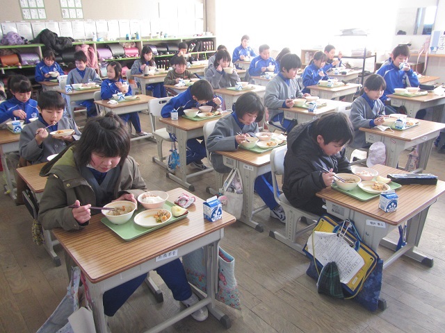 教室のそれぞれの席で前を向き黙々と給食を食べる生徒たちの写真