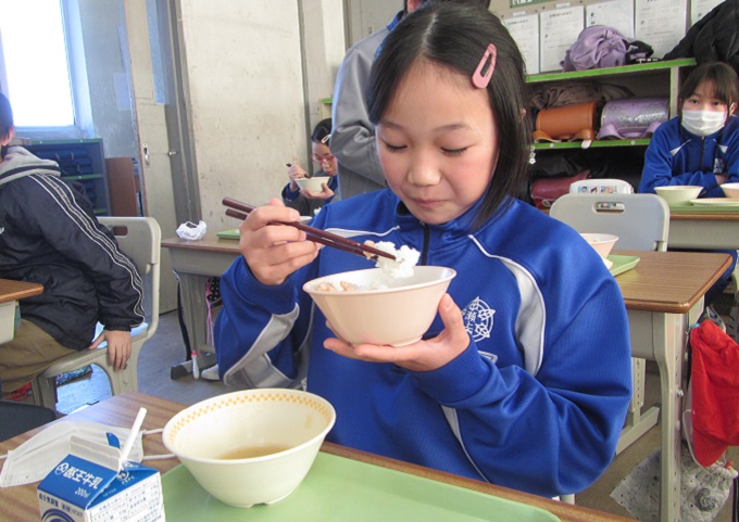 茶碗を持ち、笑顔でご飯を食べる女子生徒の写真