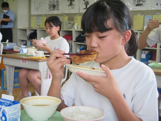 大きなとんかつを食べている女子児童の写真