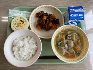 若草色のトレーの上に、ごはん、肉団子と春雨のスープ、くじらのオーロラソース和え、プリン、パックの牛乳が乗っている写真