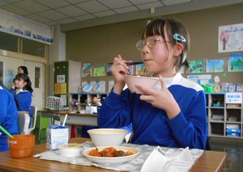 茶碗を持って給食を食べている女子生徒の写真