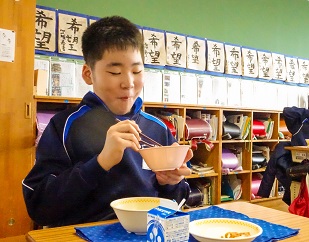 茶碗を持ってうれしそうに給食を食べている男子生徒の写真