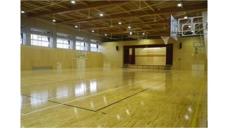板張りで左右の壁にバスケットゴール、奥に舞台が設けられた西信中学校屋内運動場の内観写真
