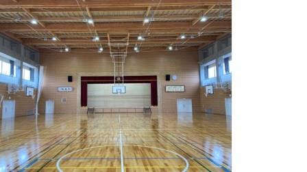 バスケットゴールが複数設置され、奥の壁には舞台がある、板張りの瀬上小学校屋内運動場の内観写真