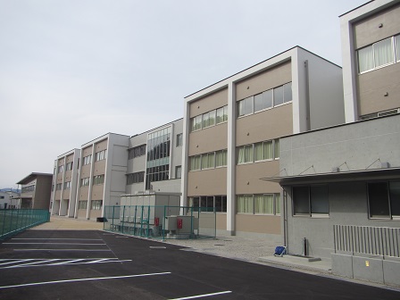 外壁が薄茶色と白で塗り分けられた、3階建ての校舎棟の外観写真