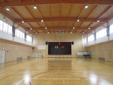 奥の壁に舞台が設けらた、板張りの屋内運動場の内観写真
