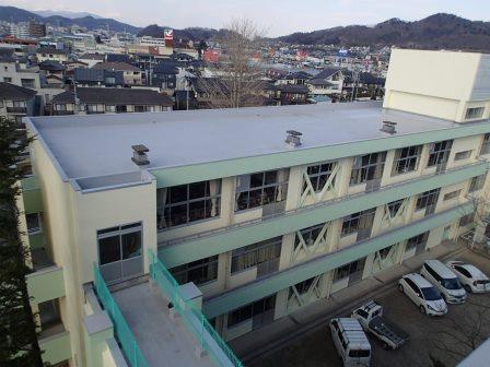 屋上防水が改修された、3階建て校舎の薄いグレーの屋上の写真
