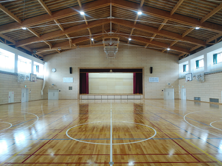 奥の壁に舞台が設けられ、左右の壁にバスケットゴールが設置された、板張りの渡利中学校屋内運動場の内観写真