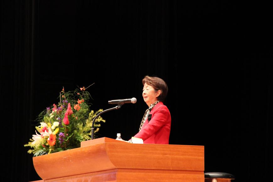 きれいなお花が飾られた演台で下重暁子さんが講演をしている様子を斜め右から写した写真