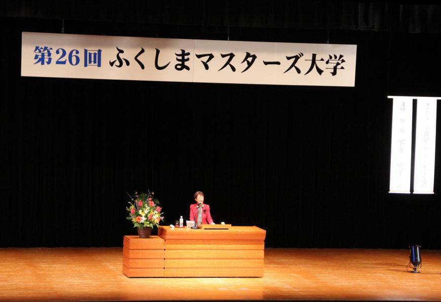 第26回ふくしまマスターズ大学の横断幕が飾られた演台で下重暁子さんが講演をしている写真