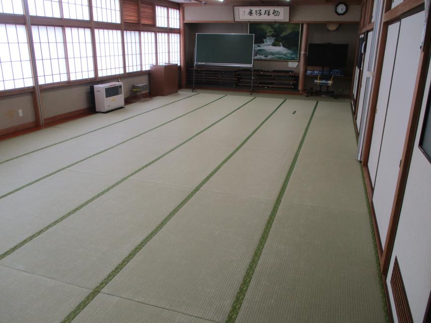 畳が並べられ、前方に黒板が置かれている広い和室の写真