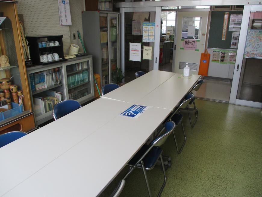 長机が2脚ずつ前後に置かれ椅子が2脚ずつ設置された談話室の奥から入り口側を写した写真