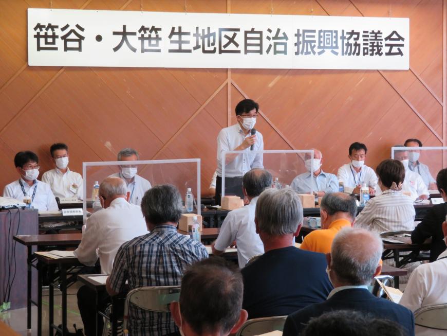 「笹谷・大笹生地区自治振興協議会」と書かれた吊り看板の下で関係者が複数名座り、市長がマイクを持って話をしているのを聞いている参加者の写真