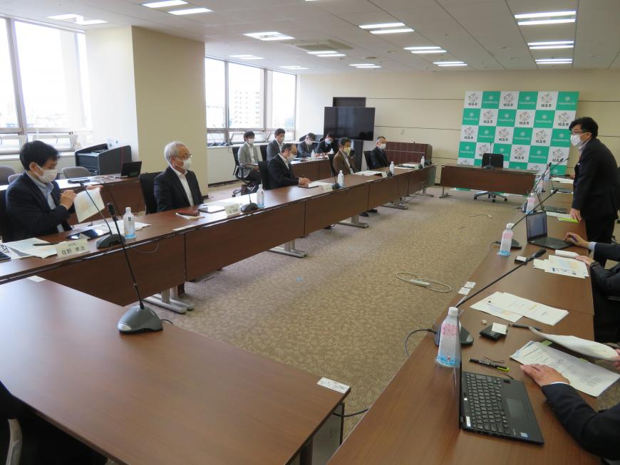 前方に福島市のバックボードの前が設置された会議室で、長机に一列に座った出席者たちに向かって立って話をしている様子の写真