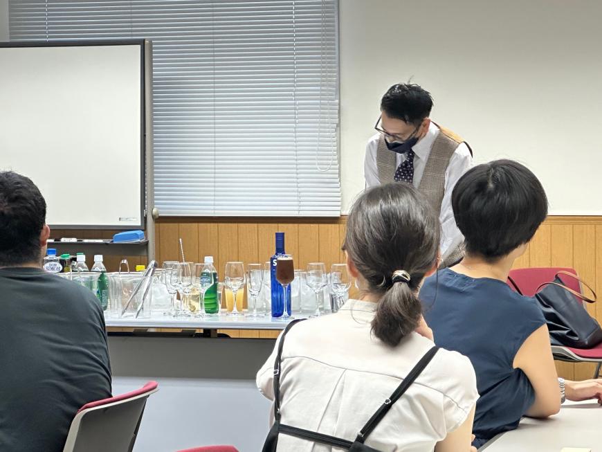 講師の先生の前の机に色々なグラスやカクテル用の道具が並べられている写真