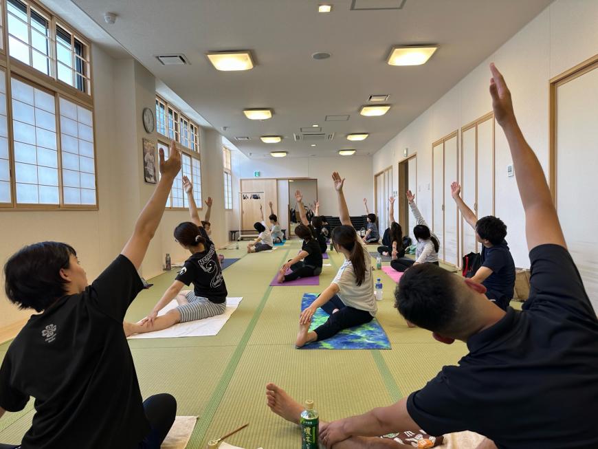細長い和室で3列に並んで座り、ヨガを楽しんでいる様子を写した写真