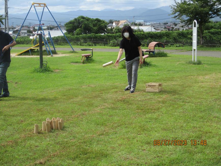 芝生に木でできたボーリングのピンのような物が並び距離を置いて女性が立っている写真