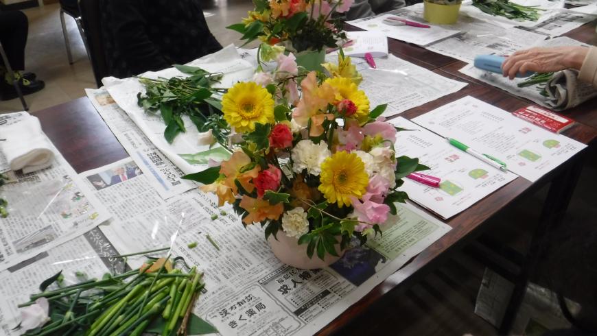 新聞紙が敷かれた長机の上に置かれた、色とりどりの花で作成したフラワーアレンジメント作品の写真