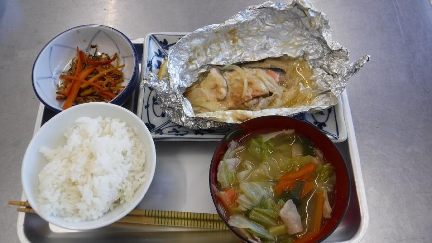 出来上がったごはん、具たくさんの味噌汁、アルミで巻かれた鮭、小鉢のきんぴらごぼうがトレーに並べられている写真