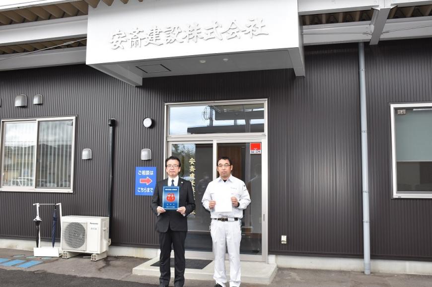 安斎建設株式会社の建物の前で男性2人が消防団協力事業所表示証を持っている写真
