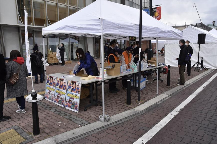 消防団員募集中のパネルが展示された白いテントの下でイベントの準備が行われている様子の写真