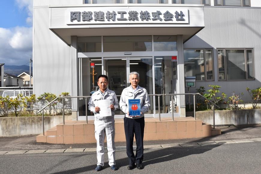 阿部建材工業株式会社の建物の前で男性2人が消防団協力事業所表示証を持っている写真
