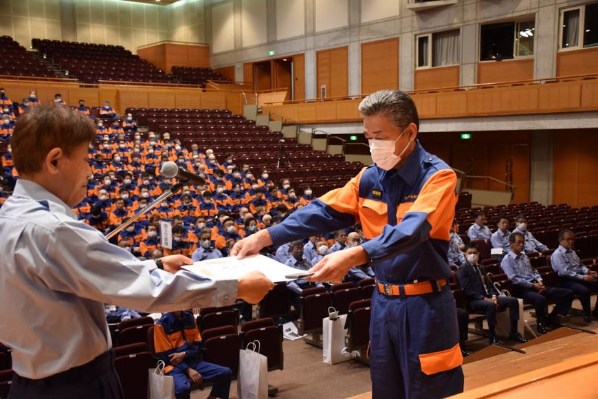 紺色とオレンジ色の入った活動服を着た男性が福島市長表彰を受け取っている様子の写真