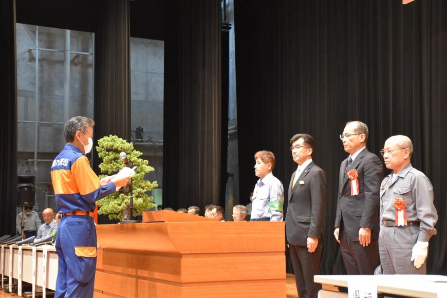 演台の前で関係者4名と活動服を着た代表者が向かい合って立ち、活動服を着た代表者が受彰者代表の謝辞を述べている様子の写真