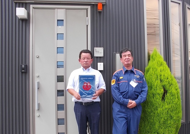 有限会社エヌオーエーの建物の前で男性が消防団協力事業所表示証を持って2人で撮影している写真