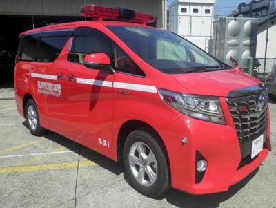 車両のルーフ部分に赤色のワイドランプを持ち、赤いボディに1本の白いラインが入った指揮車の写真