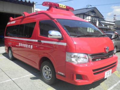 車両のルーフ部分に中央が黄色で赤色のワイドランプを持ち、赤いボディに1本の白いラインが入った指揮車の写真