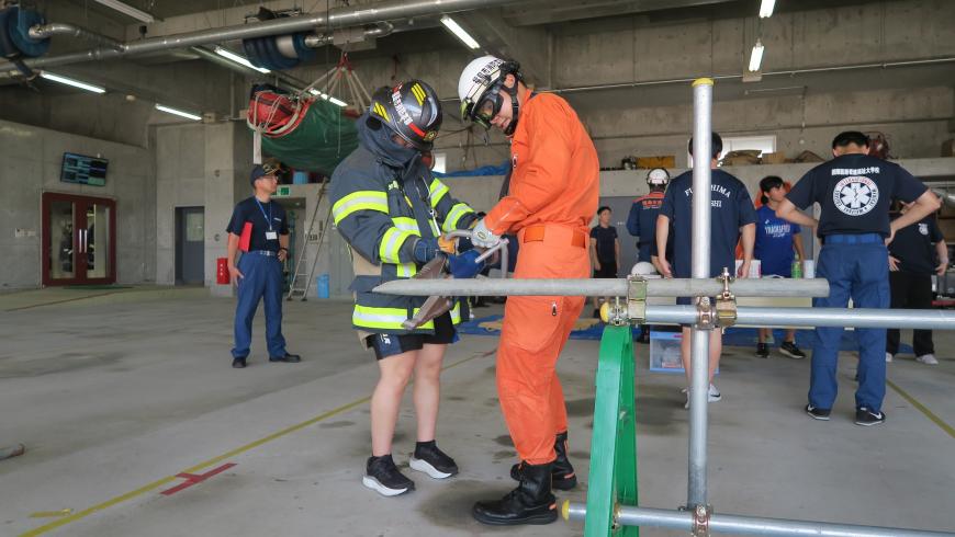 ヘルメットをかぶりオレンジの救助服を着た隊員の指導のもと、参加者が救助活動体験を行う様子の写真