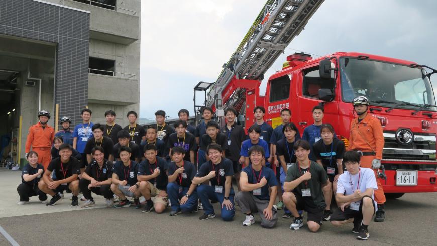 消防車の前で消防団員と参加者達が3列に並んだ集合写真
