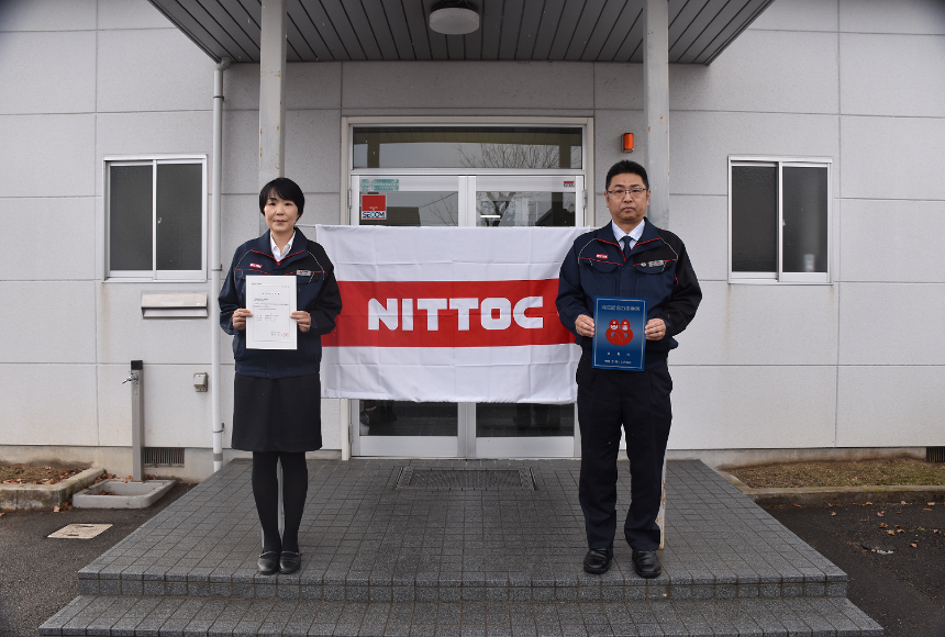 日特建設株式会社福島営業所の建物の前で社員2人が消防団協力事業所表示証を持っている写真